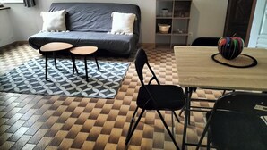 A room with a sofa, two small tables, a dining table, and a chair.