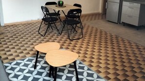 A compact kitchen with a refrigerator, a microwave, and a stove. There is a dining table with four chairs and a small fruit bowl. The floor has a geometric patterned tile design.