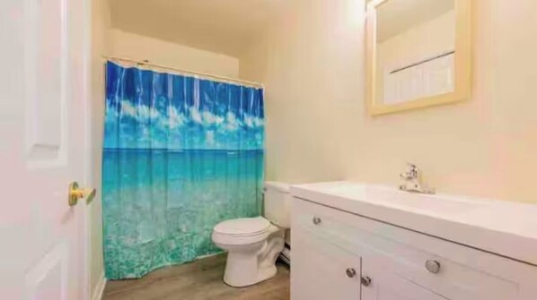Une salle de bain équipée de toilettes, d’un lavabo et d’un rideau de douche orné d’un motif représentant un océan bleu.