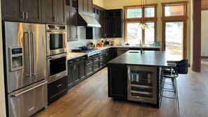 A modern kitchen with stainless steel appliances, dark cabinetry, and a large island with bar stools. - Modern 4-bed Home in Gray's Truckee Monthly Rental or Ski Lease (Truckee)