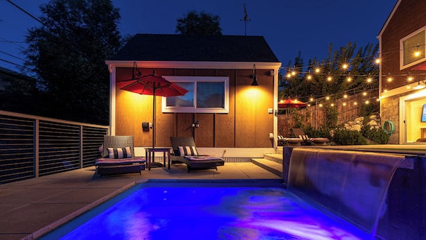 A swimming pool with a waterfall feature, surrounded by lounge chairs and a wooden deck.