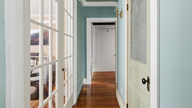 Ein Flur mit Holzboden, einer weißen Tür mit einem ornamentierten Glasfenster und einer hellblauen Wand.