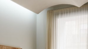 A room with a curved ceiling, a large window with sheer curtains, and a wooden panel on the wall.