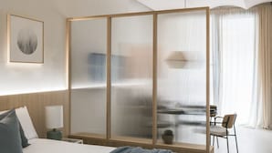 A modern hotel room with a large bed, a wooden partition, a desk, and a chair.