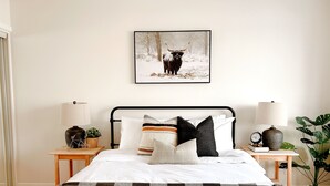 Une chambre à coucher avec un lit, une table de chevet avec une lampe, un tableau encadré au mur et une plante en pot.