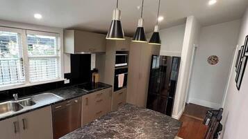 A modern kitchen with a large marble island, pendant lighting, and a view of the outdoors through the window.