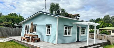 A light blue house with a covered patio, a wooden table and bench, and a fenced yard.