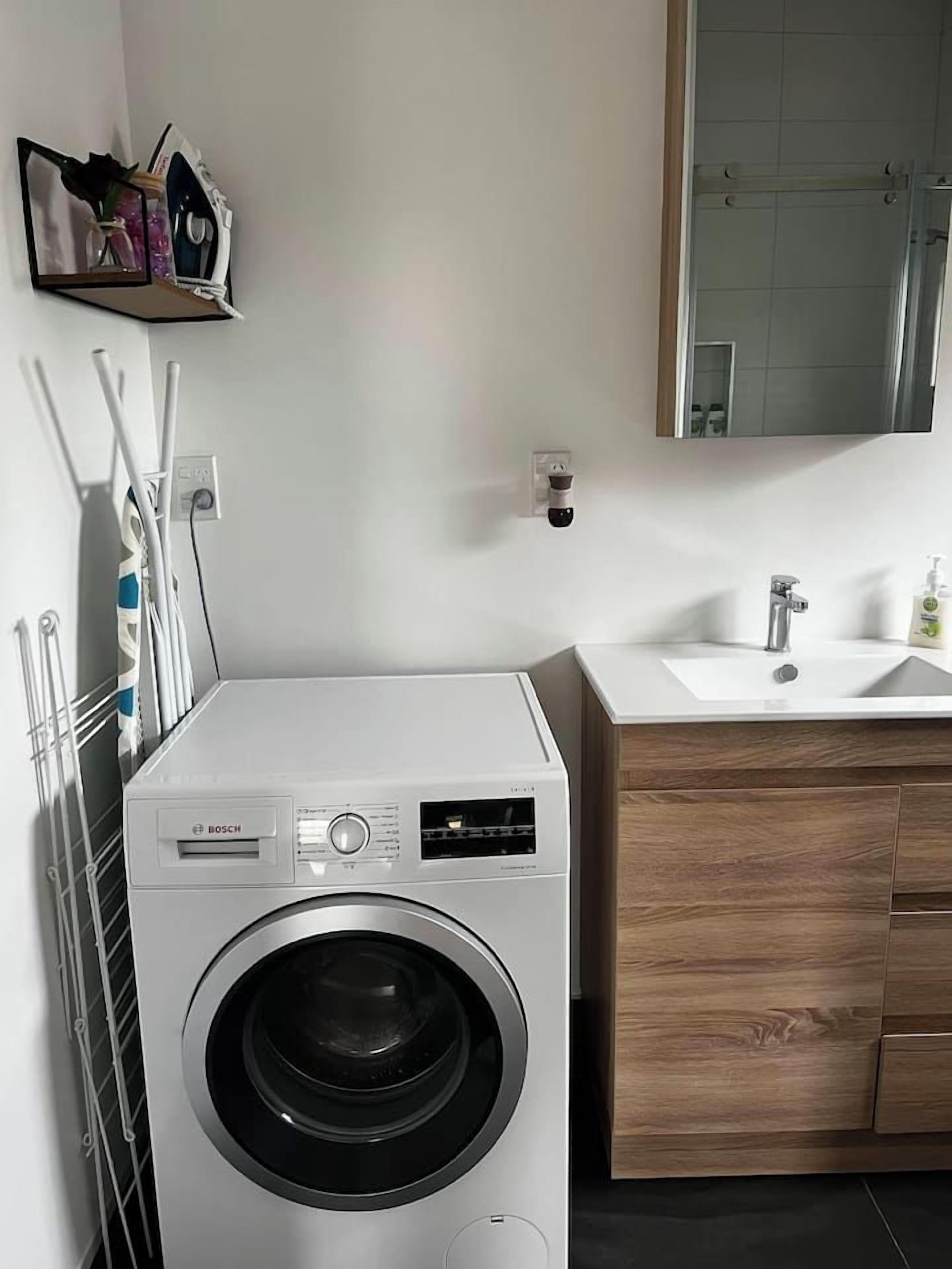 A modern bathroom with a Bosch washing machine, wooden vanity, and a mirror above the sink.