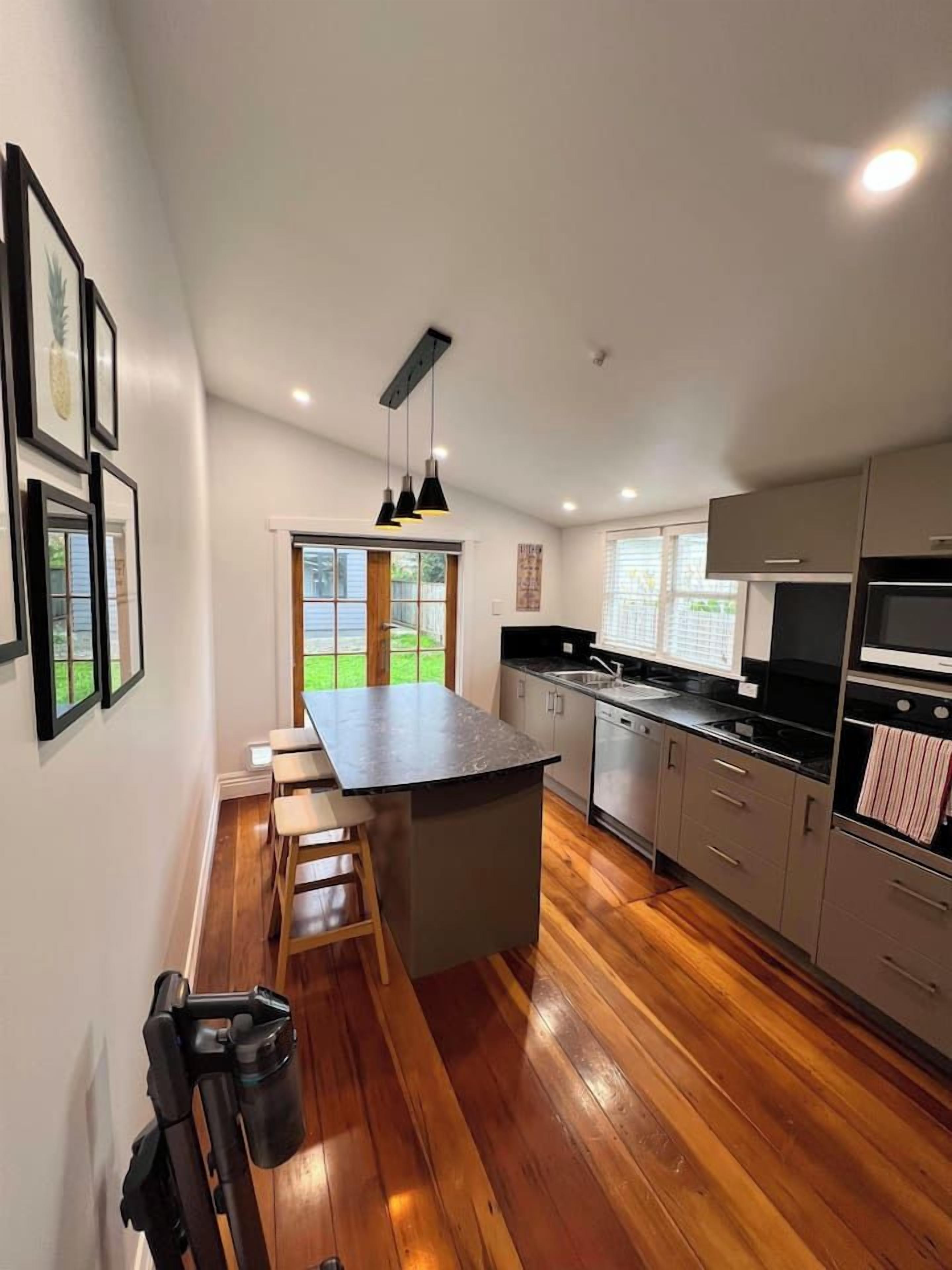 Una cocina moderna con una isla central, suelo de madera y vistas a un jardín.