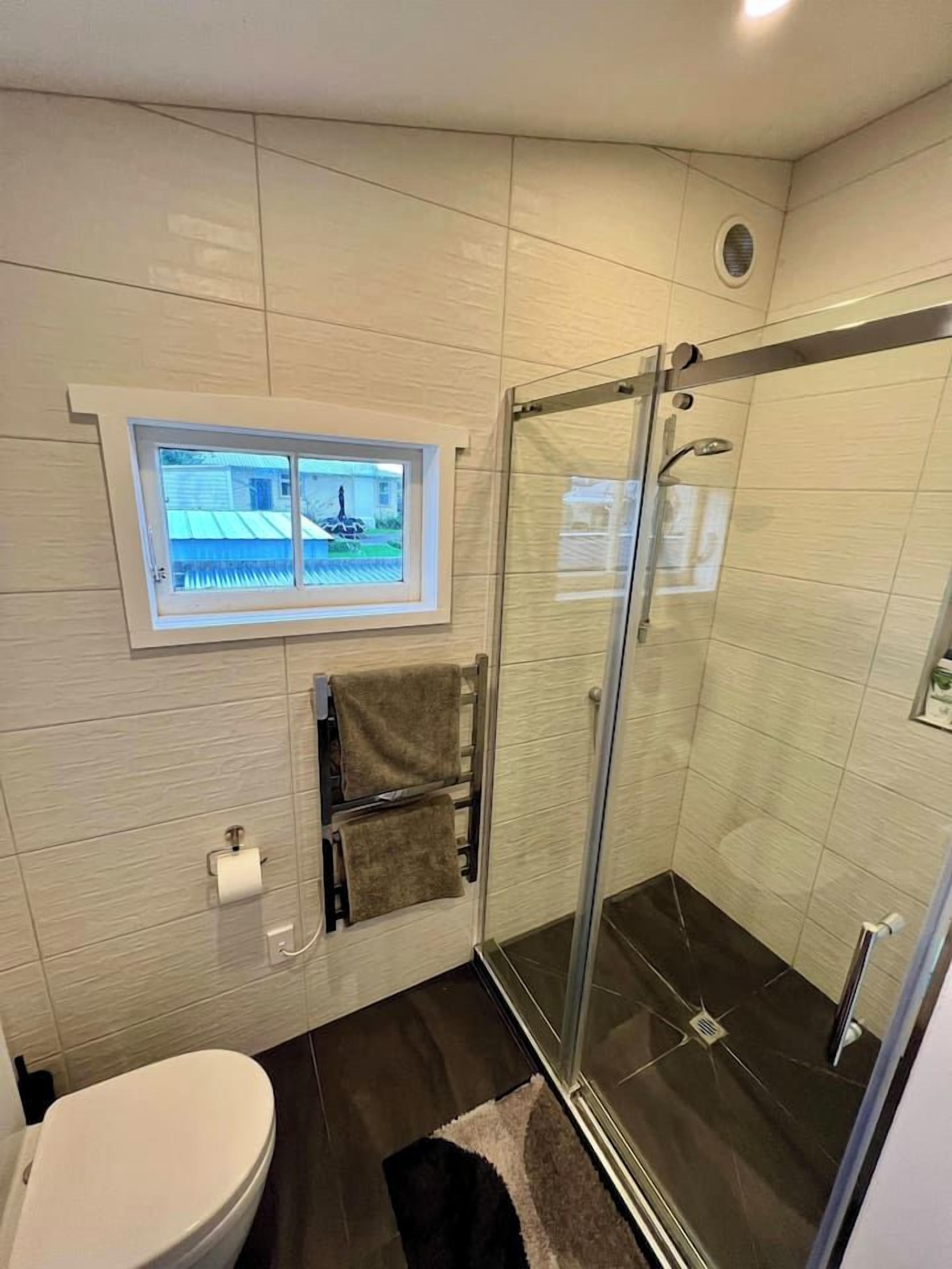 A modern bathroom with a glass-enclosed shower, a toilet, and a window providing a view of the outside.