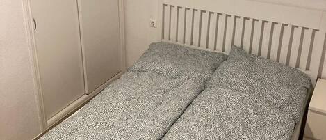 A single bed with a patterned mattress, a white headboard, and a wardrobe with two doors.