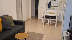 Een woonkamer met een donkere bank, een kleine ronde tafel en een eethoek met een witte tafel en stoelen.