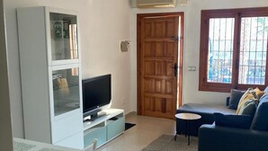 Een woonkamer met een televisie, een bank, een eettafel met stoelen en een kast.