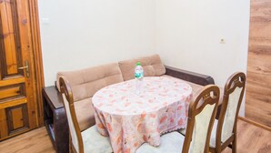 Une pièce chaleureuse avec une table ronde recouverte d’une nappe à motifs floraux, un canapé marron et une porte en bois.