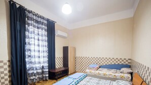 Une chambre avec deux lits, un banc en bois, un mur à carreaux et un appareil de climatisation.