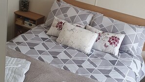 A neatly made bed with a geometric patterned bedspread, two pillows with floral designs, and a pair of folded towels on the bed. - Pet friendly Static caravan. (Dymchurch)