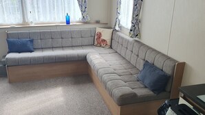 A modern living room with a grey sectional sofa, a wooden coffee table, and a small side table. - Pet friendly Static caravan. (Dymchurch)
