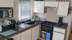 A compact kitchen with a microwave, sink, stove, and cabinets. - Pet friendly Static caravan. (Dymchurch)