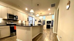 A modern kitchen with a central island, stainless steel appliances, pendant lighting, and hardwood flooring. - Charming 3-bedroom villa with WiFi and AC in marvelous Raleigh (Raleigh)