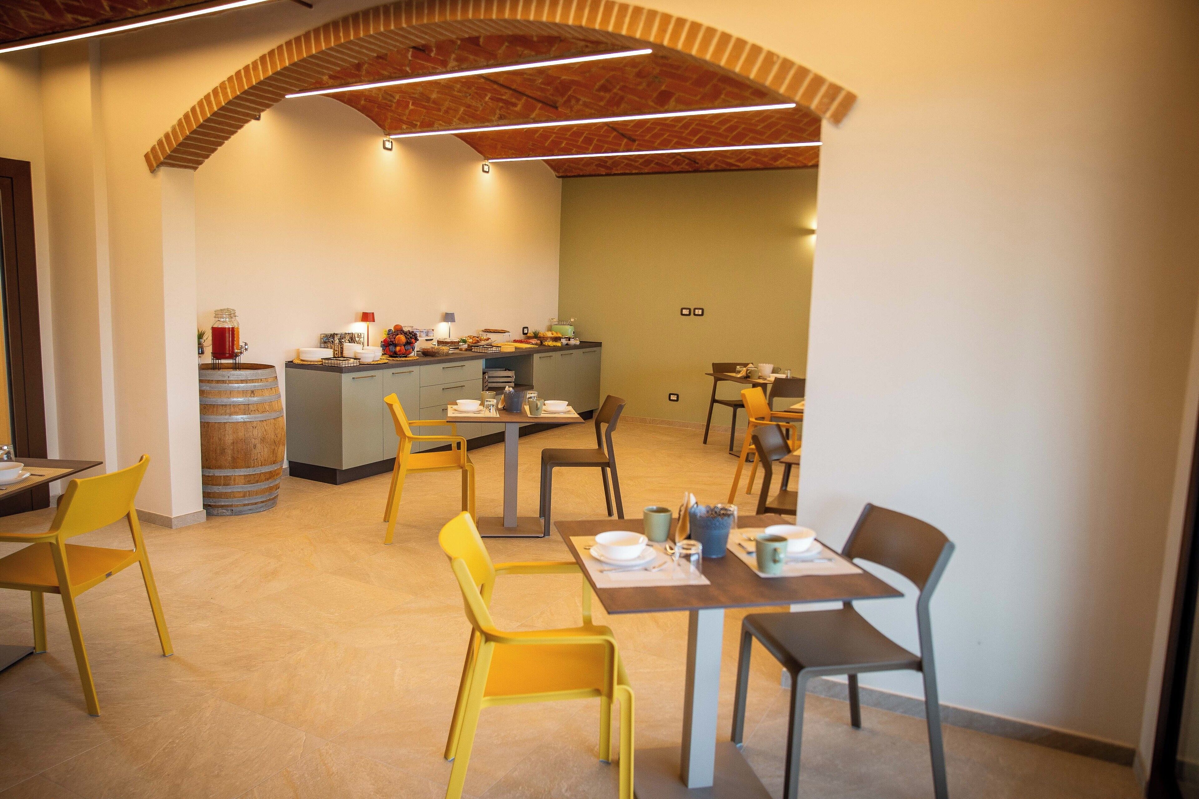 Zona pranzo con sedie gialle, una cucina sullo sfondo e un soffitto in mattoni.