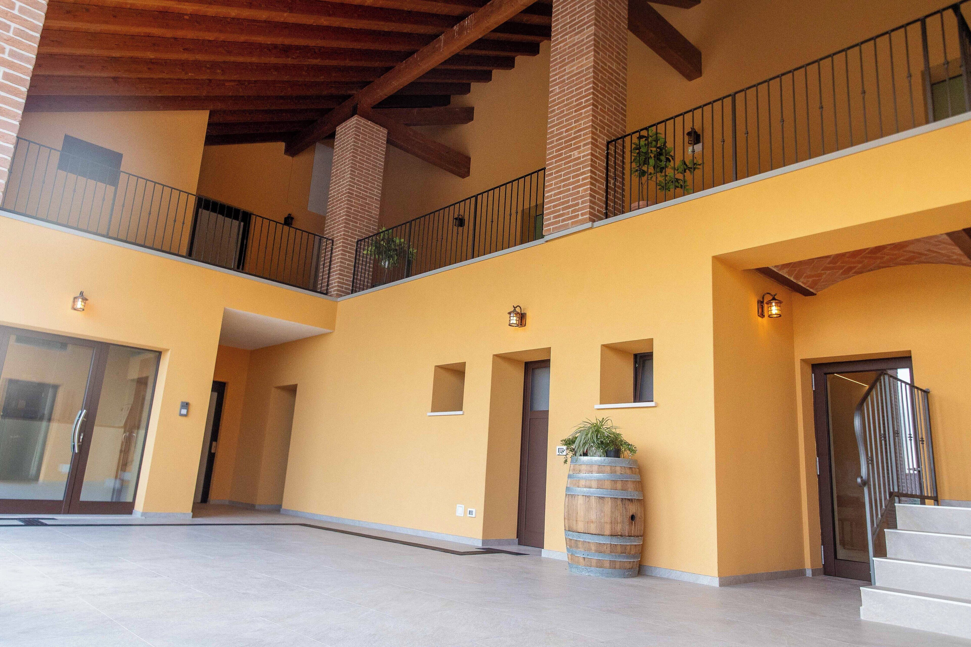 A spacious indoor area with a second-floor balcony, a large barrel planter, and a staircase leading to an upper level.
