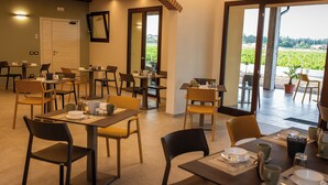 Un'area pranzo con diversi tavoli e sedie, un'ampia porta che dà sull'esterno e vista su un vigneto attraverso le porte vetrate.