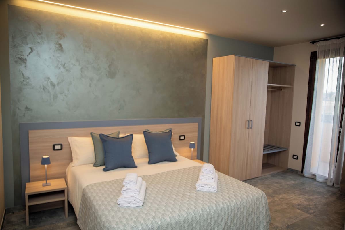 Habitación de hotel con una cama grande, dos mesitas de noche, un armario y vistas al exterior.
