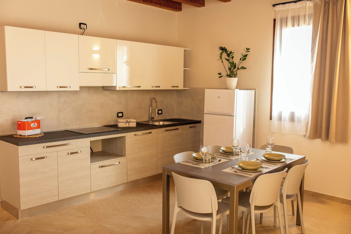 Cocina compacta con armarios blancos, horno integrado y comedor con mesa para cuatro.