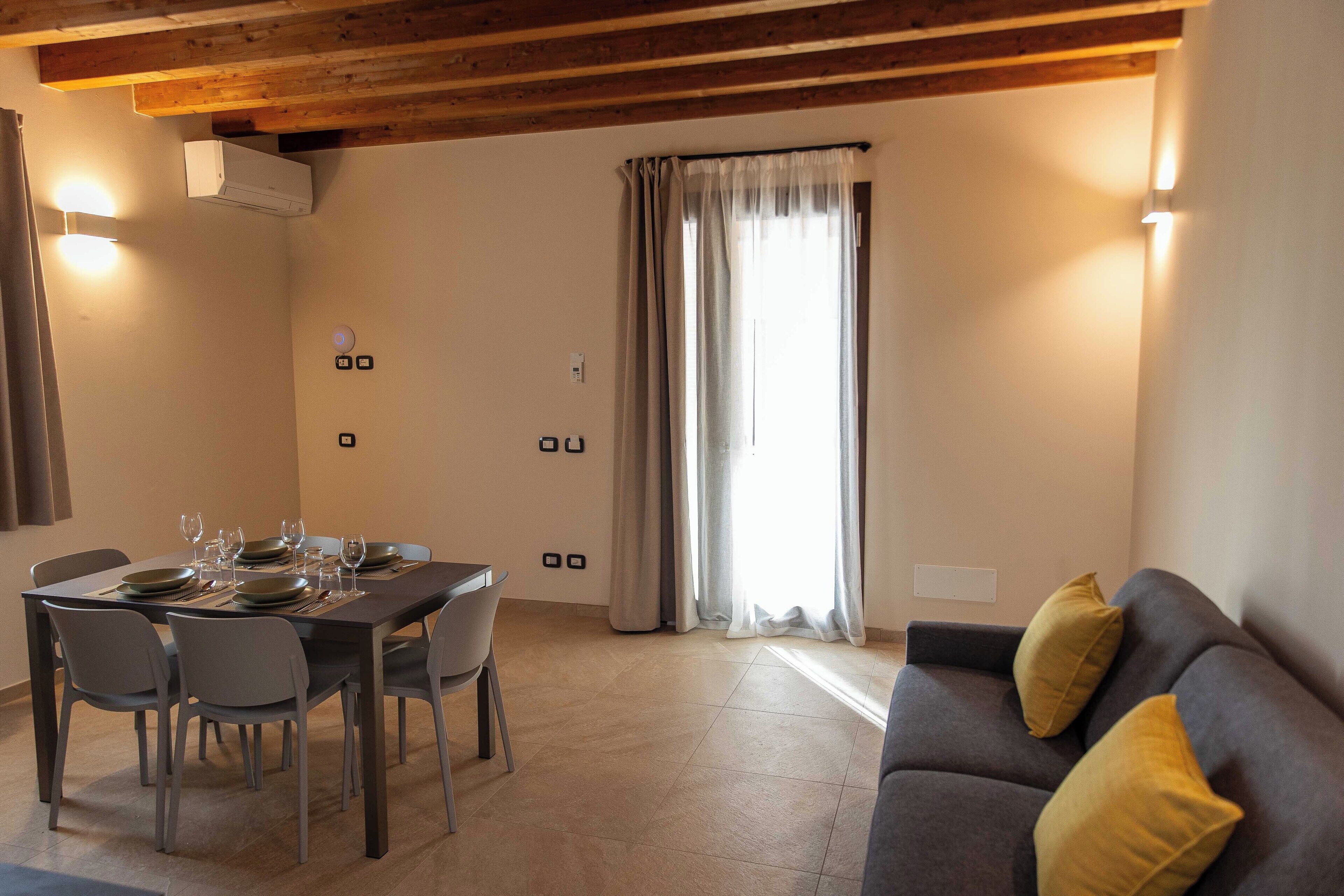 Un comedor con una mesa preparada para cuatro personas, un sofá y una ventana con cortinas.