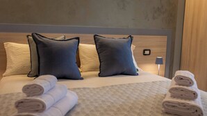 Un letto rifatto con cura, asciugamani arrotolati, due cuscini e una lampada da comodino.