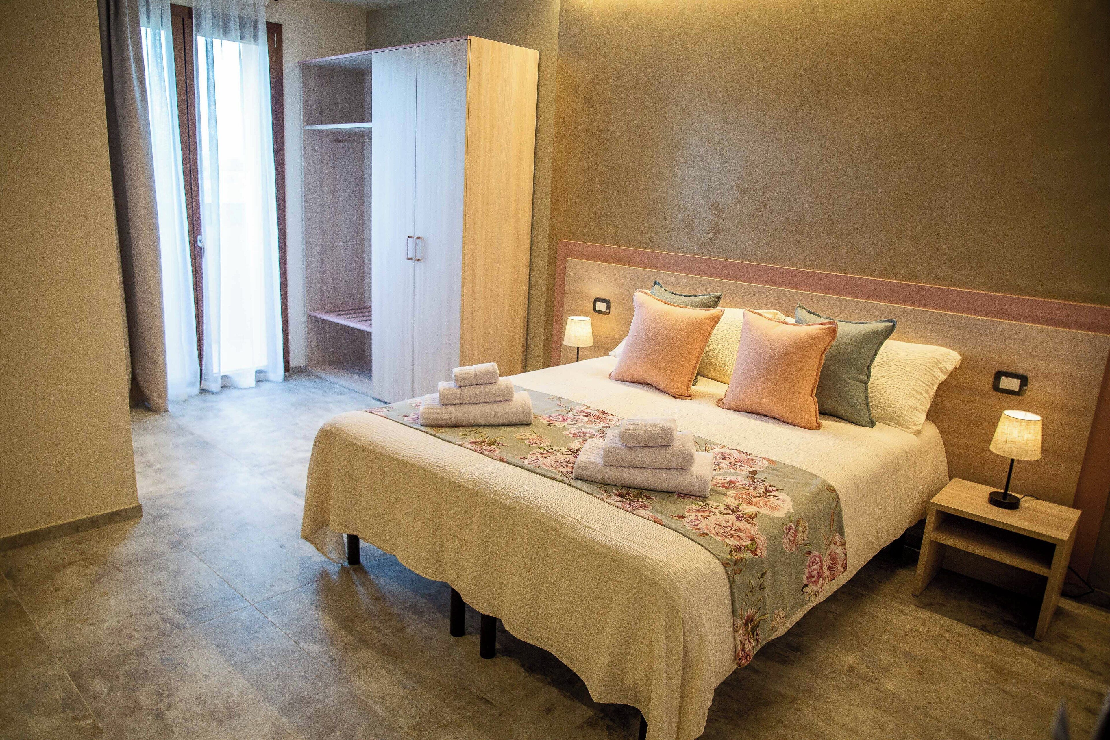 A hotel room with a bed, two bedside tables, a nightstand, a closet, and a bathroom visible through an open door.