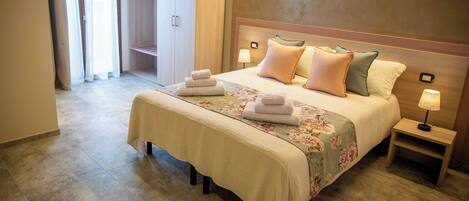 A hotel room with a bed, two bedside tables, a nightstand, a closet, and a bathroom visible through an open door.