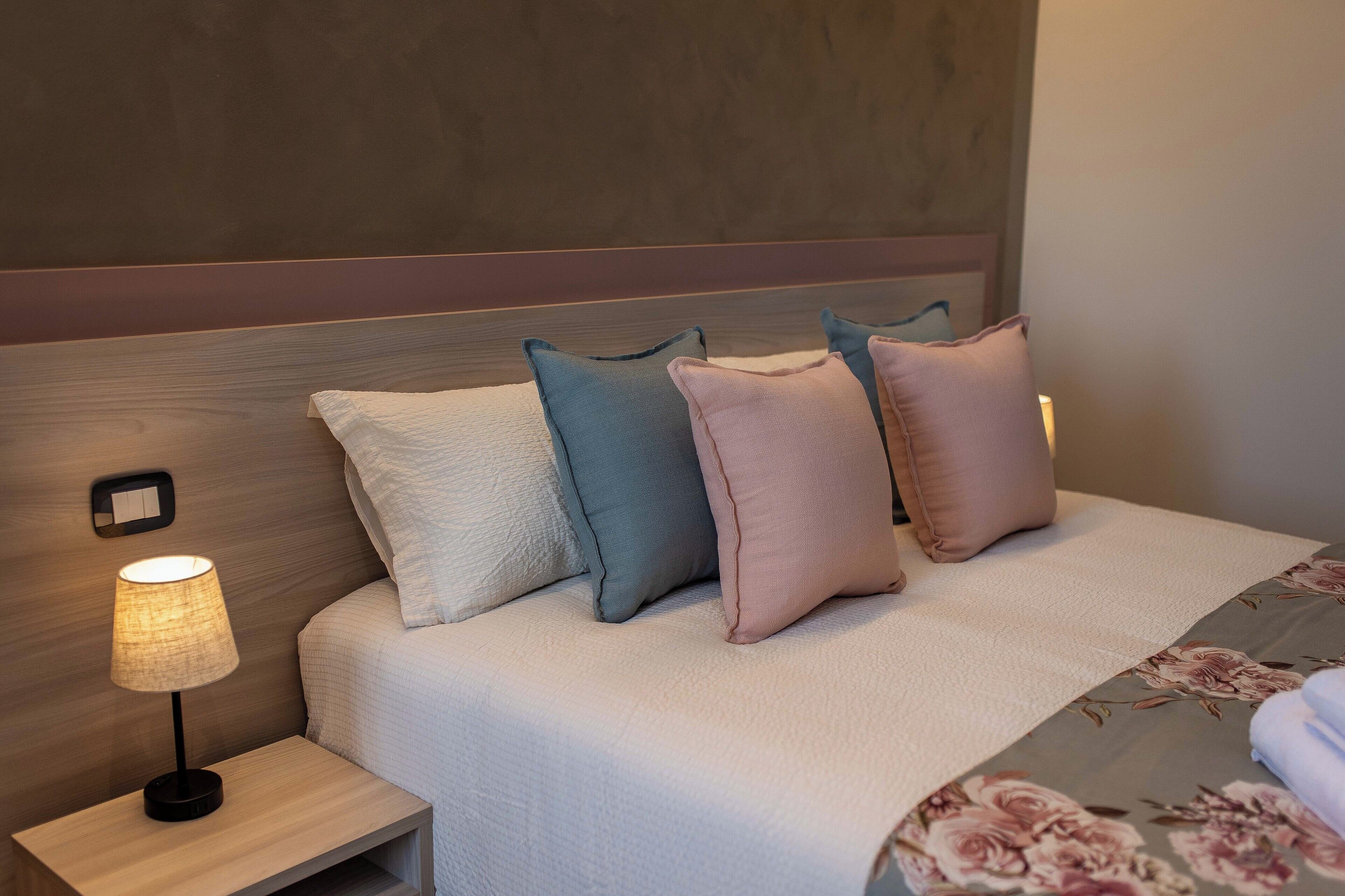 A neatly made bed with a floral-patterned bedspread, a bedside lamp, and multiple pillows in various colors.