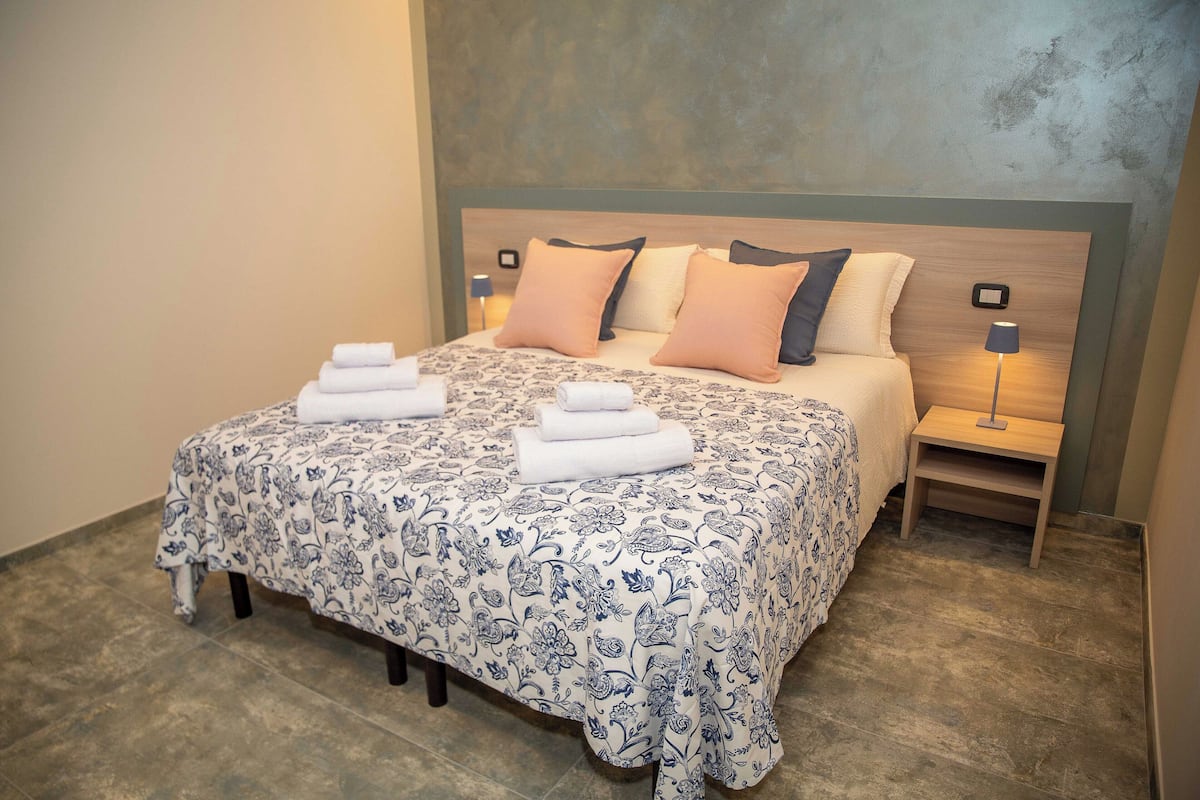 Una cama bien hecha con una colcha estampada de flores, dos mesitas de noche con lámparas y una pared texturizada detrás de la cama.