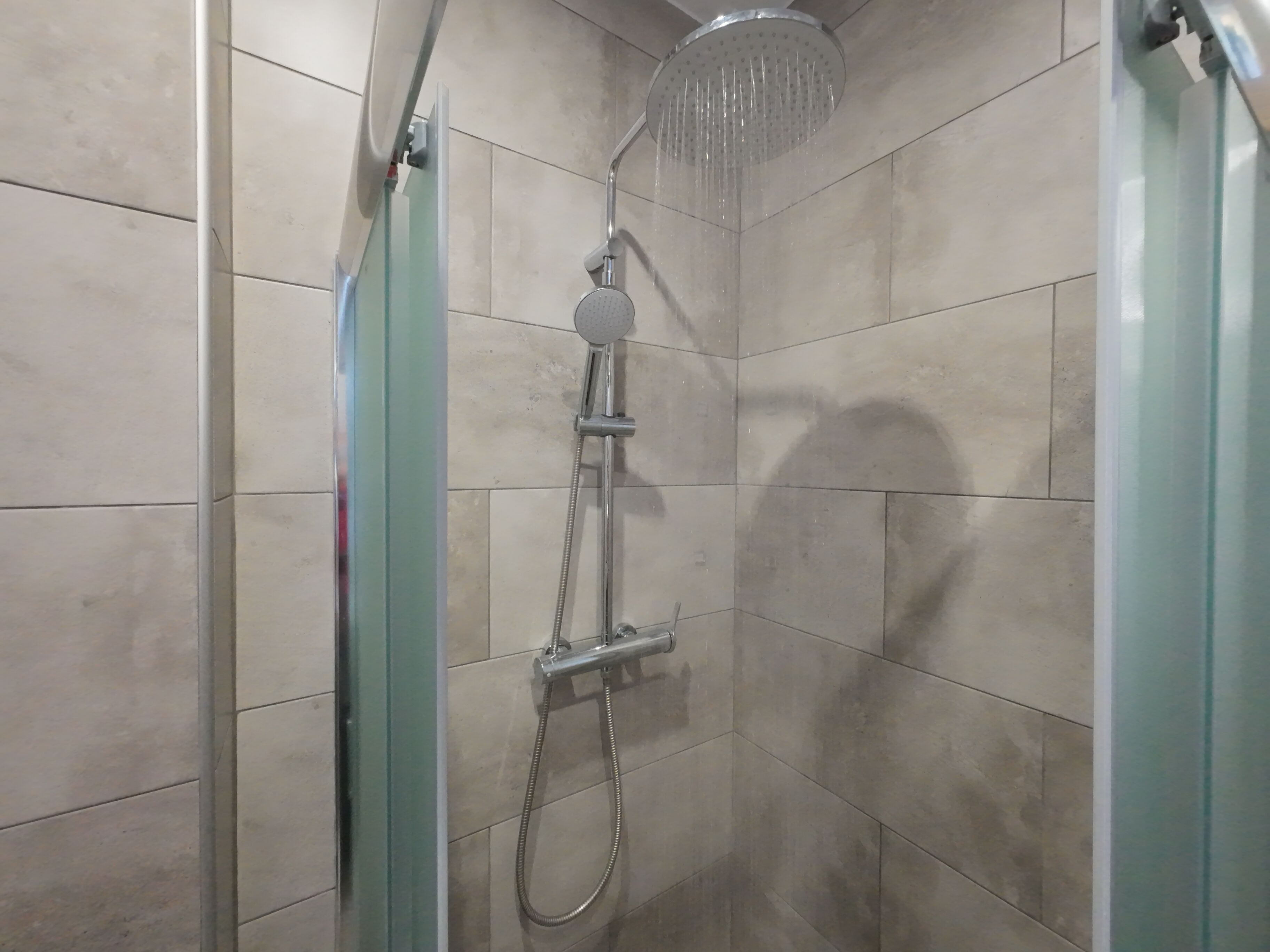 A shower with a handheld showerhead and a fixed overhead showerhead, both mounted on a tiled wall.