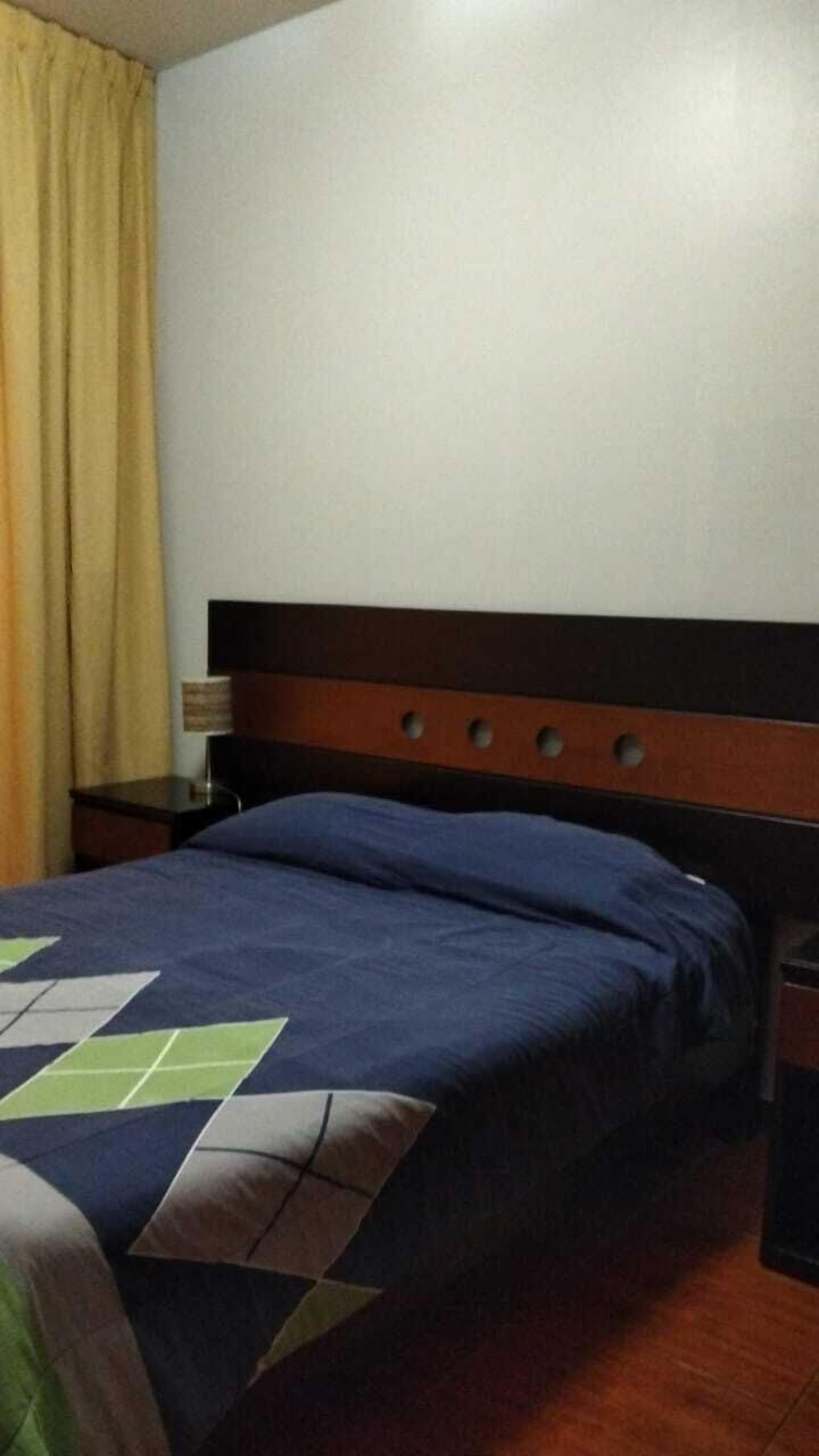 Una habitación de hotel con cama, mesita de noche y l ámpara.