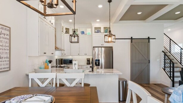 A modern kitchen with white cabinetry, a stainless steel refrigerator, and pendant lighting. - Barefoot Breeze w/Pool, Kayaks, Fireplace (Winchester)