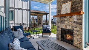 A covered patio area with a stone fireplace, a sofa, and a table. - Barefoot Breeze w/Pool, Kayaks, Fireplace (Winchester)
