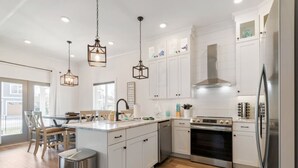 A modern kitchen with white cabinets, stainless steel appliances, and wooden flooring. - Barefoot Breeze w/Pool, Kayaks, Fireplace (Winchester)
