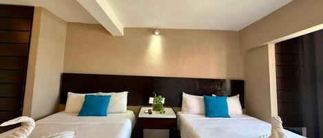 Quarto de hotel com duas camas, uma mesa pequena e uma mesinha de cabeceira.