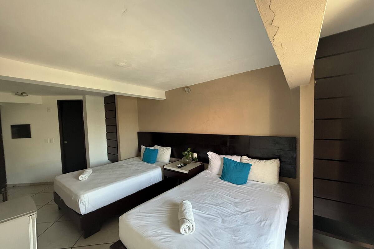 A hotel room with two beds, a nightstand, a TV, and a door leading to another room.