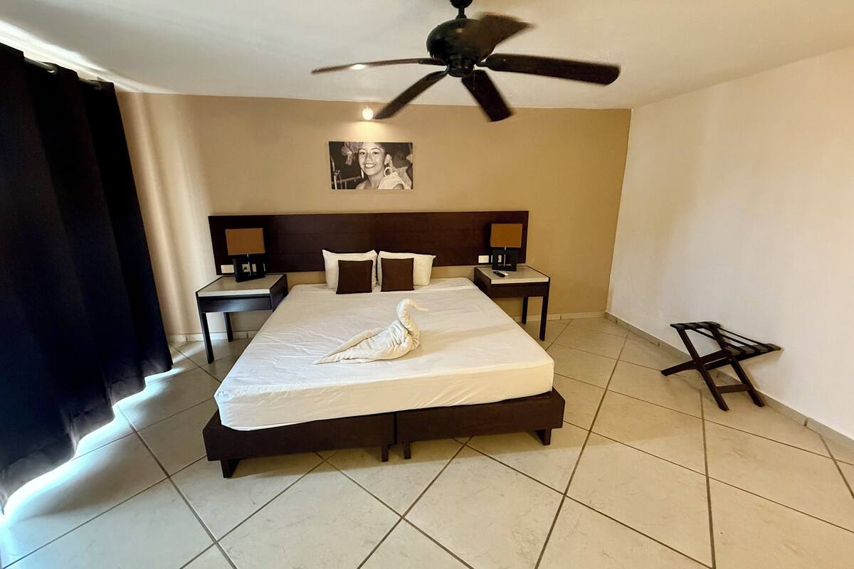 A hotel room with a large bed, a ceiling fan, two bedside tables with lamps, and a framed picture on the wall.