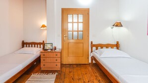 A small, cozy room with two single beds, a wooden door, a nightstand with a lamp, and a small rug on the floor. - Guesthouse `Hapa të Lehtë` -  Room 1 - Pro Bono by PikHost (Shkodër)