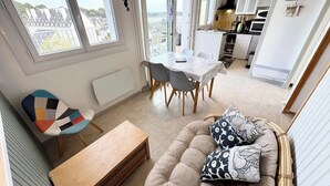 Moderni olohuone, jossa on sohva, puinen sohvapöytä ja värikäs tuoli. Taustalla näkyy ruokailutila, jossa on pöytä ja tuolit, sekä keittiö.