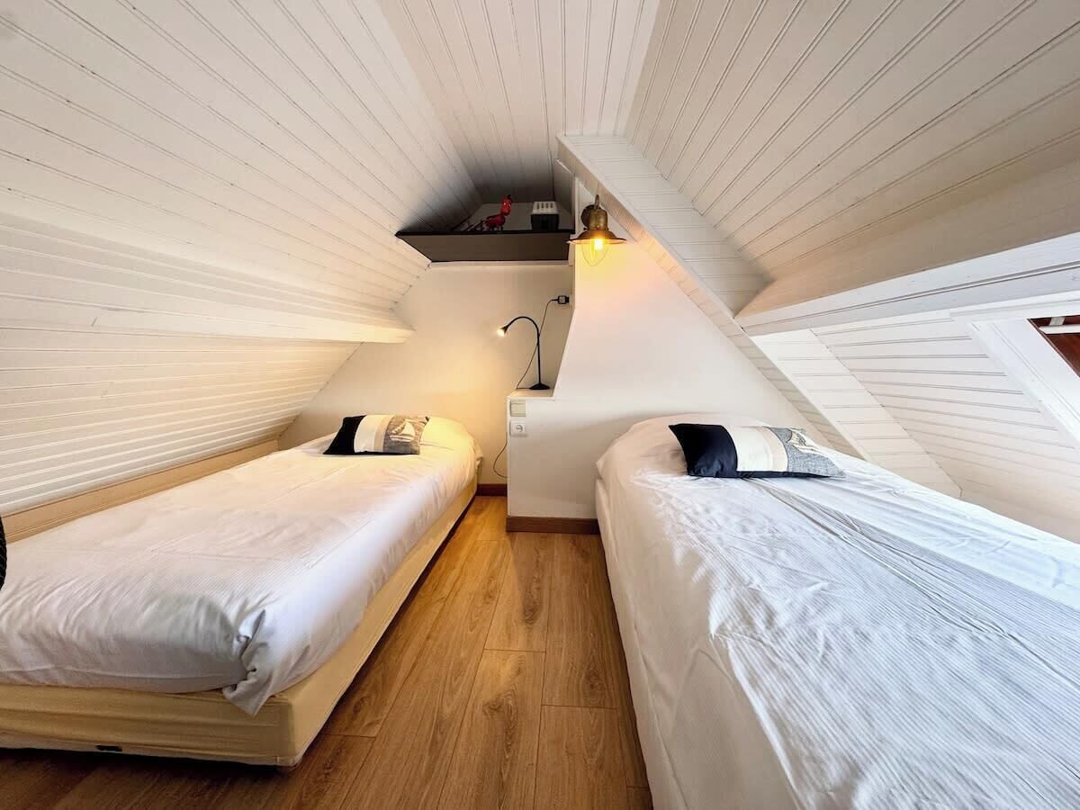 Une petite chambre accueillante avec deux lits simples, un plancher en bois et un plafond en pente.