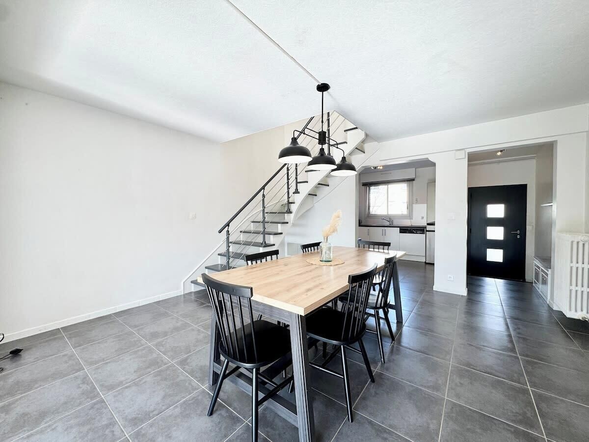 Et rummeligt køkken med moderne design, et spiseområde med et træbord og stole, samt en trappe op til et højere niveau.