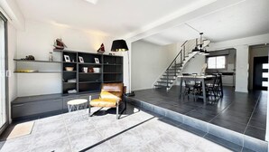 Un amplio espacio de sala con diseño moderno, que incluye un sillón de cuero, una mesa de comedor y una escalera que sube a un nivel superior.