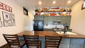 Una cocina con una isla central, dos taburetes de bar, un refrigerador, un microondas y un fregadero.
