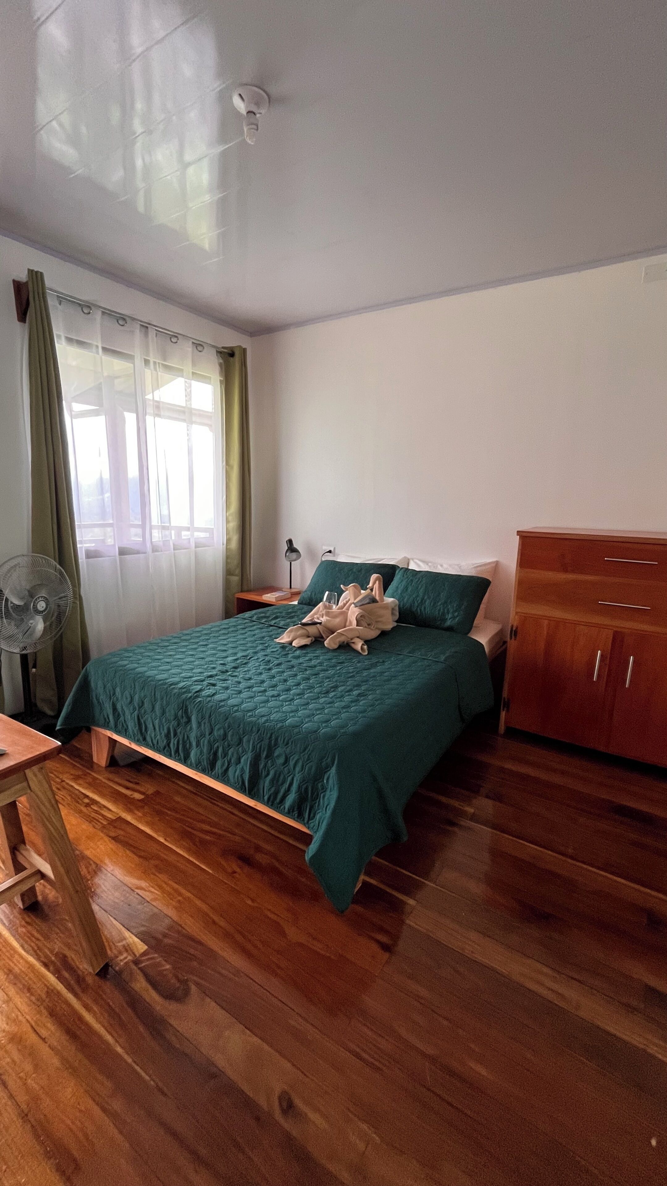 Ein Schlafzimmer mit Bett, Holzboden, einem Holzschrank, einem Schreibtisch und einem Fenster mit Vorhängen.