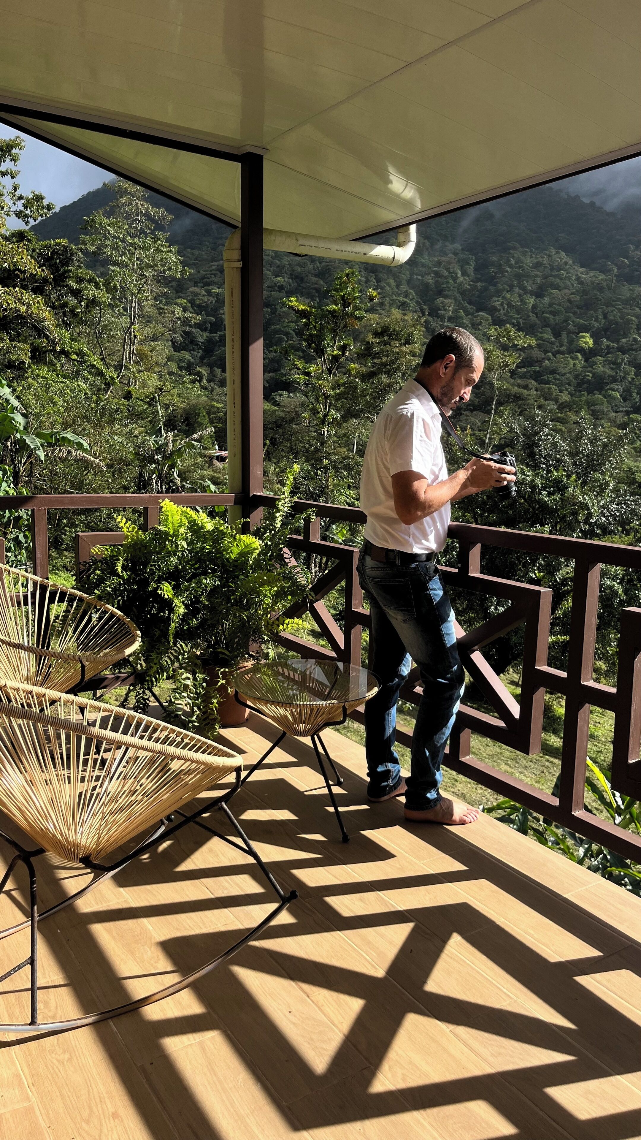 Un hombre en un balcón con una cámara, contemplando un exuberante paisaje boscoso.